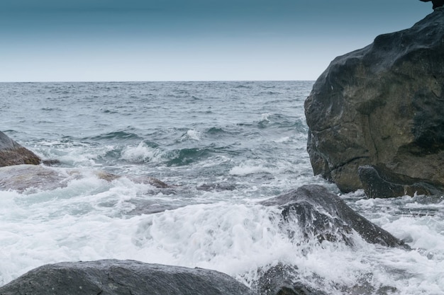 Wellen schlagen bei bewölktem Wetter gegen Felsen an der Küste des Ozeans