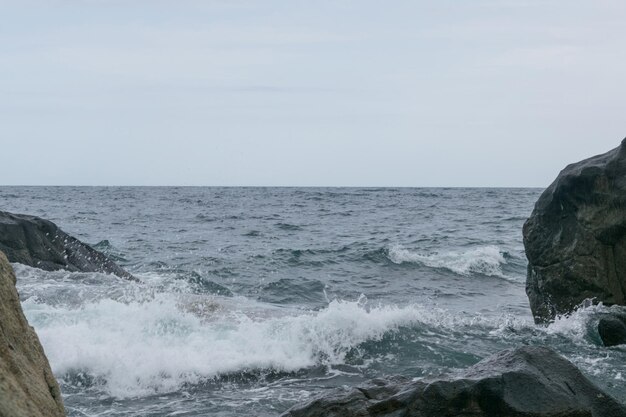 Wellen schlagen bei bewölktem Wetter gegen Felsen an der Küste des Ozeans