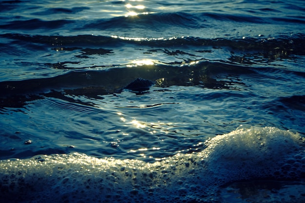 Wellen und Schaum am Strand bei Sonnenuntergang.