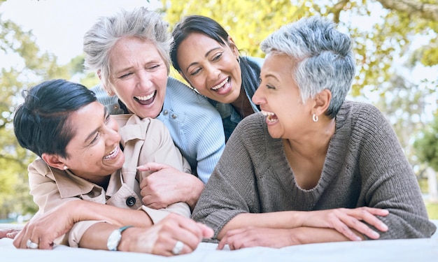 Wellness glückliche und pensionierte Freundinnen lachen im Park für Gruppenbindung und entspannenden Lebensstil Lustiger Witz und Lächeln älterer Menschen in interrassischer Freundschaft in der Natur zusammen