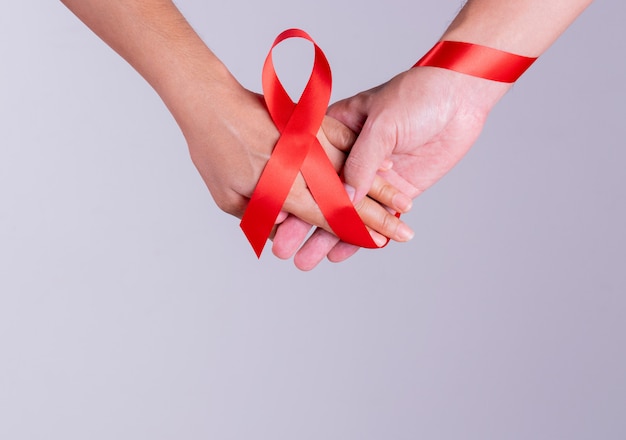 Welt-AIDS-Tag. Mann- und Frauenhändchenhalten zusammen mit AIDS-Rotband