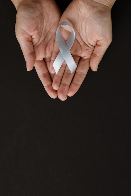 Welt-Hirntumor-Tag. Die Hände einer Person halten ein graues Band auf schwarzem Hintergrund. Dies wird beobachtet