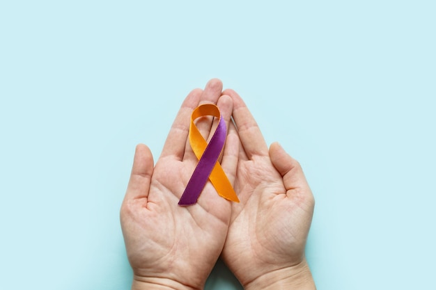 Welt-Psoriasis-Tag Die Hände der Frau halten ein lila orangefarbenes Band Behandlung von Hautkrankheiten
