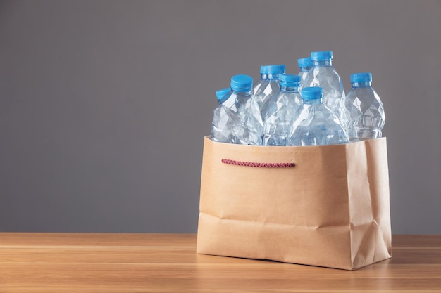 Welt- und Umweltkonzept retten Gebrauchte blaue Plastikflasche in brauner Papptasche auf Holzschreibtisch und dunklem Hintergrund Kann für die Wiederverwendung von Recycling- und Umweltkonzepten verwendet werden