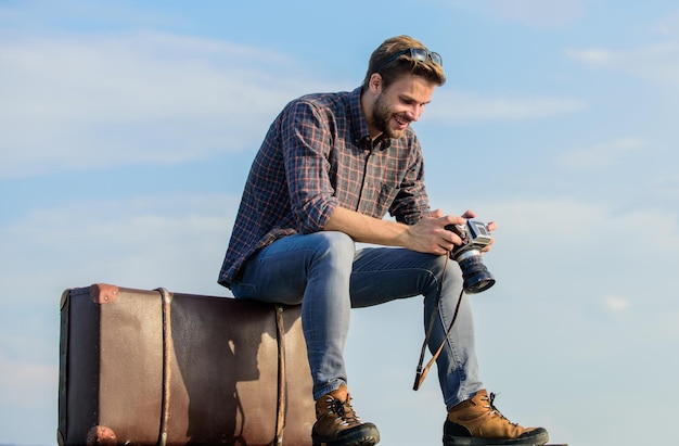 Welt zu sehen Journalist mit Kamera Geschäftsreise Macho Mann Tourist sitzen auf Tour Tasche Reisenden warten auf Flug Bewegen Sie sexy Mann Himmelshintergrund männlichen Modestil, der so trendy aussieht