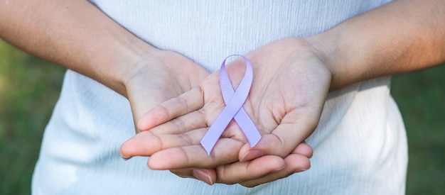 Weltkrebstag (4. Februar). Frauenhand, die Lavendelviolettband für die Unterstützung des lebenden Lebens und der Krankheit hält.
