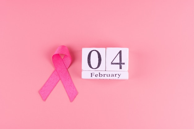 Weltkrebstag mit Kalender vom 4. Februar und Pink Ribbon zur Unterstützung von Menschen, die leben und krank sind. Gesundheitskonzept