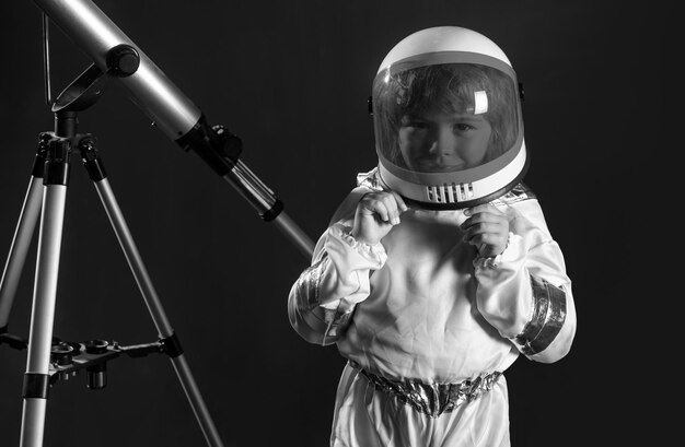 Weltraumkinder-Kosmonauten-Konzeptporträt eines positiven kleinen Jungen mit einem Teleskop und einem Helm