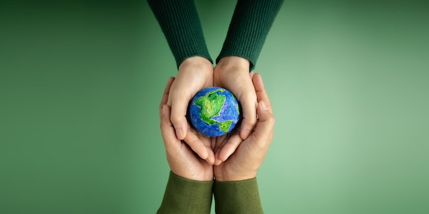 Welttag der Erde Konzept Grüne Energie ESG Erneuerbare und nachhaltige Ressourcen Umweltschutz Hände von Menschen, die einen handgefertigten Globus umarmen, um den Planeten zusammen zu schützen Top View