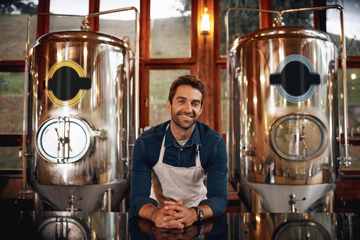 Foto wenn sie bier wollen, haben wir es porträt eines fröhlichen jungen barkeepers, der sich an die bartheke lehnt und darauf wartet, dass kunden in einer bierbrauerei dienen