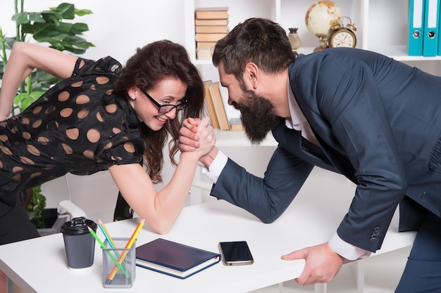 Wer ist stärker. Bärtiger Mann und sexy Frau Armdrücken im Büro. Beziehung am Arbeitsplatz. Wettbewerbsverhältnis. Beziehung zwischen Geschäftspartnern. Professionelles Paar. Beziehung oder Rivalität.