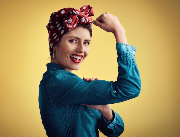 Wer sagt, dass Frauen nicht stark sein können? Studioporträt einer attraktiven jungen Frau, die ihren Bizeps beugt, während sie vor einem gelben Hintergrund steht