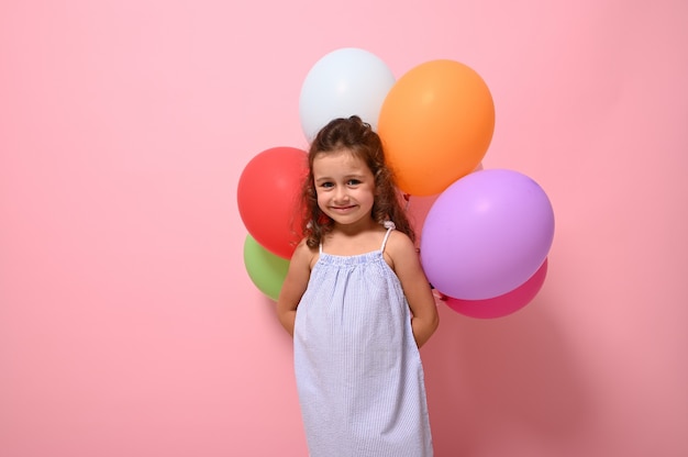 Werbefotografie mit süßem Baby im Sommerkleid mit bunten Luftballons, posiert vor rosa Hintergrund, Kopierraum