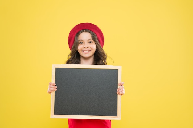 Werbetafel für die Förderung zurück zur Schule Schuleinkaufsverkauf Kind auf gelbem Hintergrund glückliches Mädchen in französischer Baskenmütze kleines Mädchen Kind mit Schule Backboard Copy Space Verlagsgeschäft