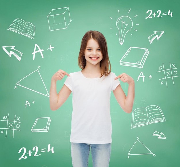 Werbung, Geste, Bildung, Kindheit und Menschen - lächelndes Mädchen im weißen T-Shirt, das mit dem Finger auf sich selbst über grünem Brett mit Kritzeleien zeigt