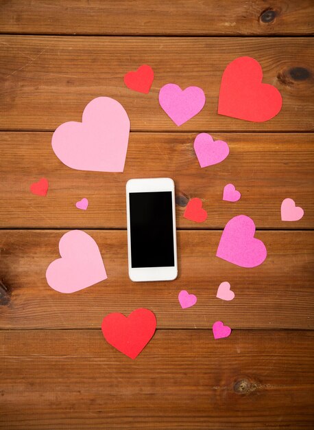 Werbung, Romantik, Valentinstag und Feiertagskonzept - Nahaufnahme von Smartphone und Herzen auf Holz