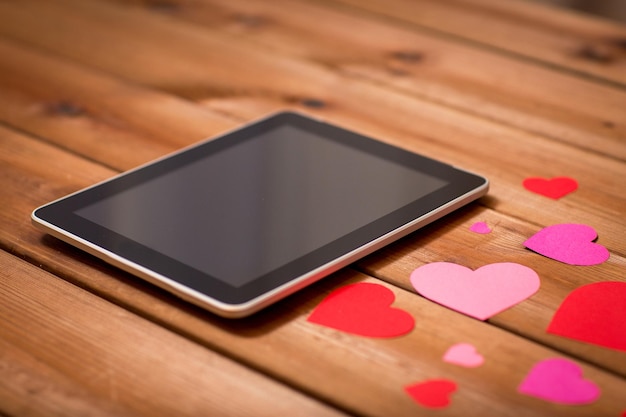 werbung, romantik, valentinstag und feiertagskonzept - nahaufnahme von tablet-pc-computer und herzen auf holz