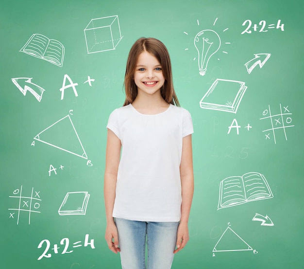 werbung, schule, bildung, kindheit und leute - lächelndes kleines mädchen im weißen leeren t-shirt über grüner tafel mit gekritzelhintergrund