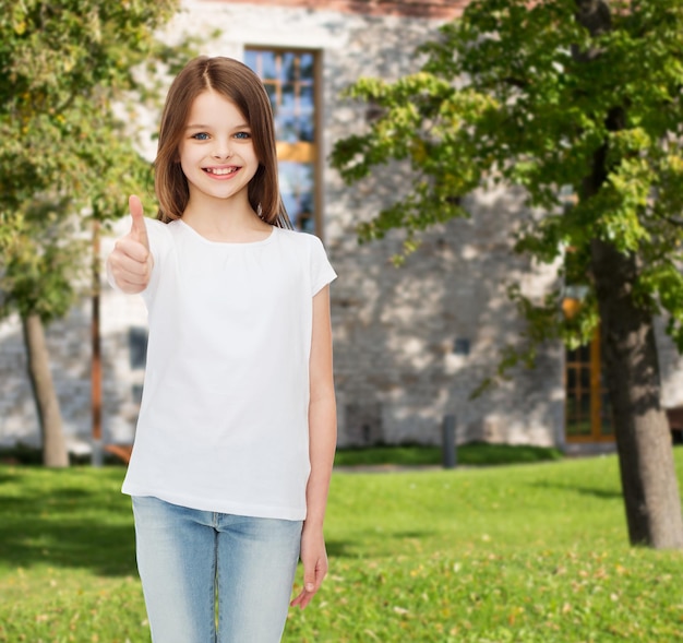 Werbung, Sommerferien, Gesten, Kindheit und Menschen - lächelndes kleines Mädchen im weißen T-Shirt, das Daumen nach oben über dem Campus-Hintergrund zeigt