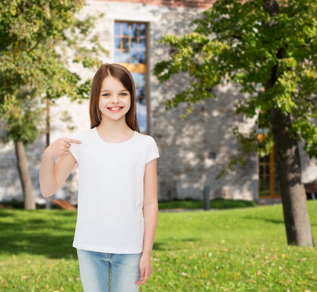 Werbung, Urlaub, Geste, Kindheit und Menschen - lächelndes Mädchen im weißen T-Shirt, das mit dem Finger auf sich selbst über dem Campus-Hintergrund zeigt