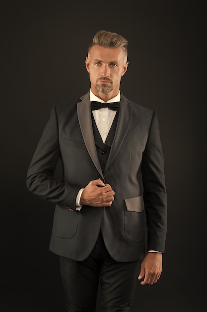 Werden Sie die Klassiker schätzen, bärtiger Mann mit formellem Aussehen, Hipster mit schwarzem Hintergrund, brutaler Mann im Smoking-Anzug, Klassiker kann den Mann schlauer aussehen lassen, schwarze Krawatte, Modegeschäft, Kauf von Kleidung, Männerbekleidung, Konzept.