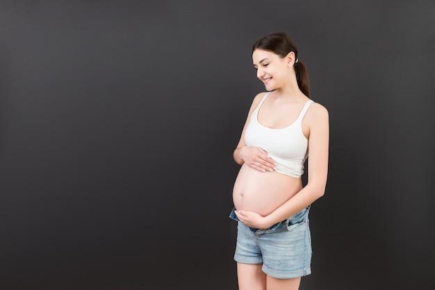 werdende Mutter in geöffneten Jeans, die ihren nackten schwangeren Bauch vor buntem Hintergrund mit Kopierraum zeigt Schwangerschaftskonzept