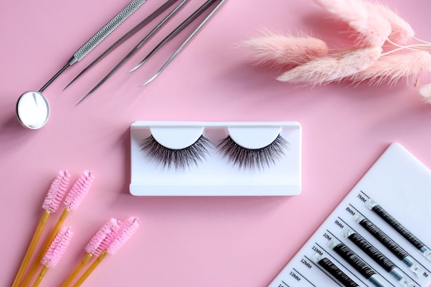 Werkzeuge für die Wimpernverlängerung auf trendigem pastellrosa Hintergrund Falsche Wimpern Pinzette und Bürsten Schönheitssalon Make-up-Kosmetik Draufsicht flach liegend