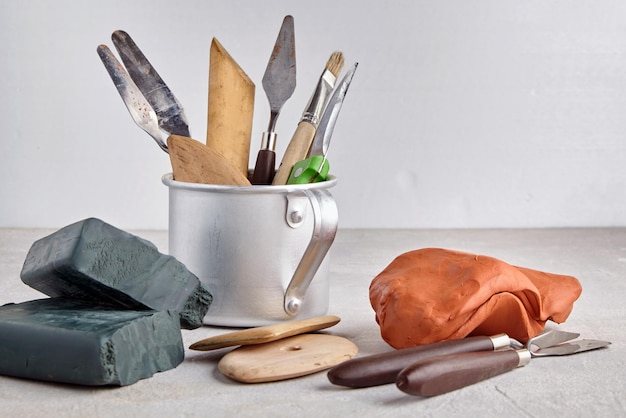 Foto werkzeuge zum formen und modellieren in einem aluminiumbecher und stücke aus plastilin und ton auf hellem werkstatthintergrund