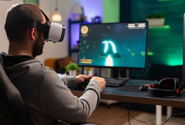 Wettbewerbsfähiger Spieler, der E-Sport-Meisterschaft mit drahtlosem Technologienetzwerk spielt Professioneller Mann mit VR-Headset und Online-Weltraum-Shooter-Wettbewerb auf einem leistungsstarken Computer