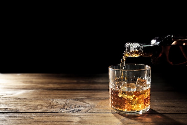 Whiskey in Glas auf Holztisch gießen, Nahaufnahme