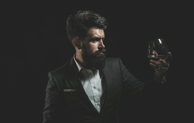 Whiskey oder Brandy oder Cognac trinken Eleganter und stilvoller Mann in klassischer Kleidung, der ein Glas mit Wiskey in der Hand hält Stilvoller reicher Mann, der ein Glas alten Whiskey hält