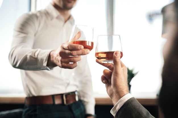 Whisky caro. Cerca de dos empresario sosteniendo vasos con whisky caro bebiendo después del trabajo