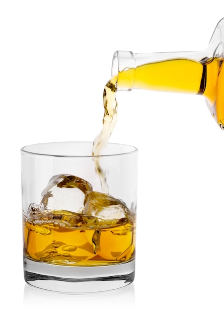 Whisky dorado se vierte de la botella en un vaso con hielo