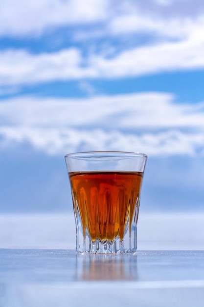 Whisky enfriado en un vaso sobre una superficie de hielo contra un cielo borroso Bebida alcohólica de naranja en un vaso Espacio de copia Vista lateral Vertical