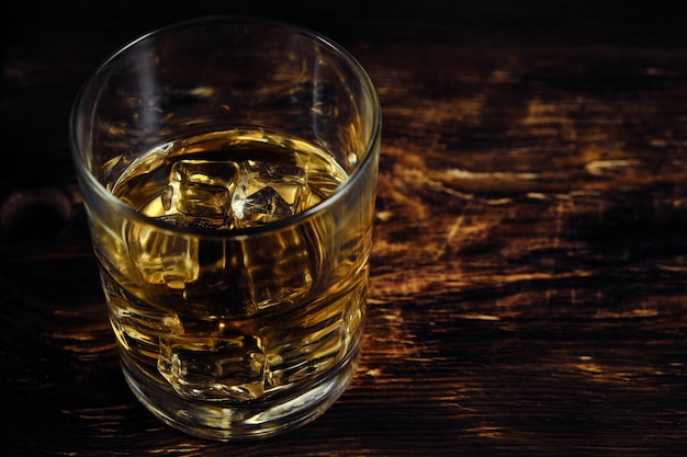 Whisky enfriado en vidrio con cubitos de hielo sobre fondo de madera.