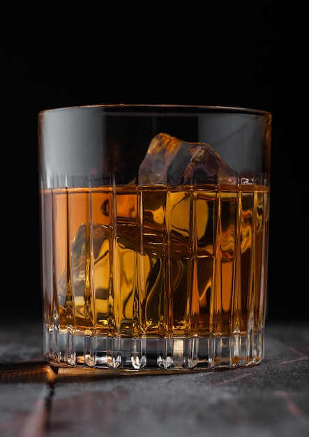 Whisky escocés de malta en vaso de cristal con cubitos de hielo sobre fondo de mesa de madera. Macro