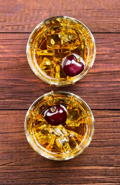 Whisky con hielo y cereza en dos vasos.