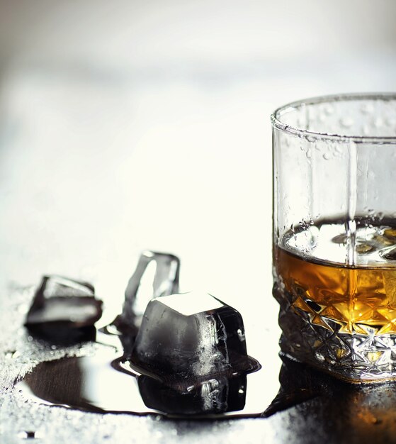 Whisky con hielo con vaso. Cubos de hielo sobre una mesa de madera y un vaso con alcohol fuerte refrigerado. Mesa con whisky americano, bourbon y cartas.