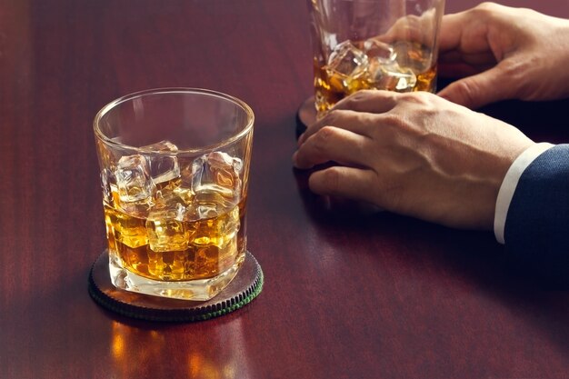 Whisky en mesa de madera y hombre de negocios con whisky en mano