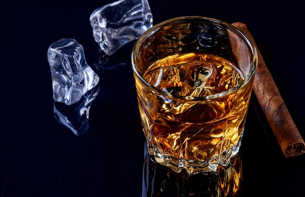 Whisky mit Eis oder Brandy im Glas mit Zigarre auf schwarzem Hintergrund