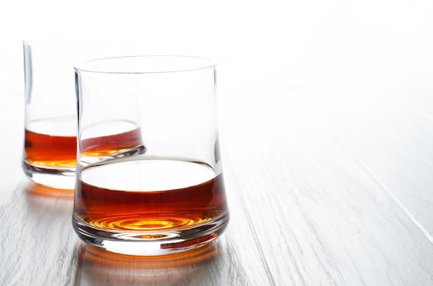 Whisky o coñac o brandy en un vaso de vidrio sobre una mesa de madera blanca.