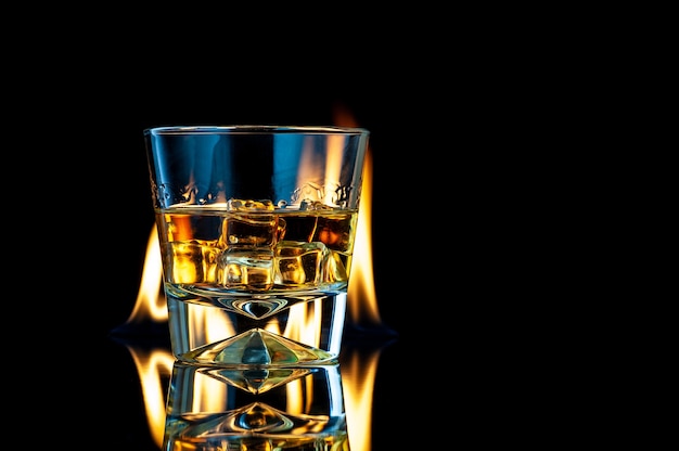 Whisky oder Bourbon in einem transparenten Glas mit Eiswürfeln auf einem schwarzen mit Feuer