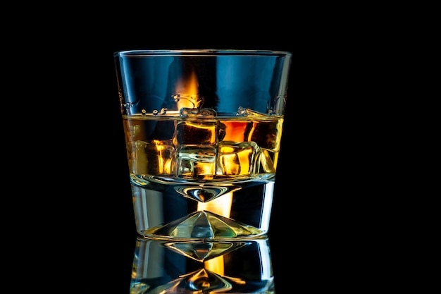 Whisky oder Bourbon in einem transparenten Glas mit Eiswürfeln auf einem schwarzen mit Feuer