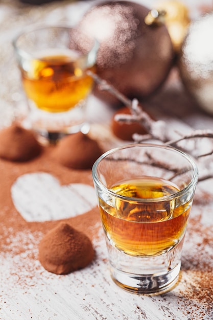 Whisky oder Likör, Trüffelschokoladen in Kakaopulver und Weihnachtsdekorationen auf weißem hölzernem Hintergrund.