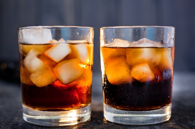 Whisky oder Rum mit Cola und Eis in Gläsern auf dunklem Hintergrund