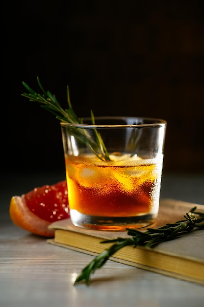 Whisky-Sauer-Cocktail mit Rum-Eis-Grapefruit und Rosmarin im Schnapsglas auf Buch Alkohol-Cocktail