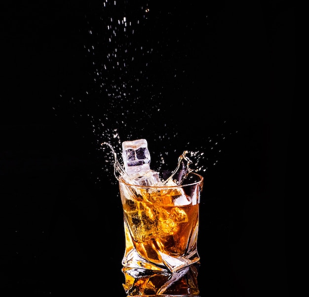 Whisky con splash sobre fondo negro, brandy en un vaso