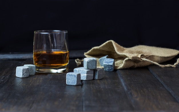 Whisky en un vaso con piedras para enfriar bebidas en una mesa de madera