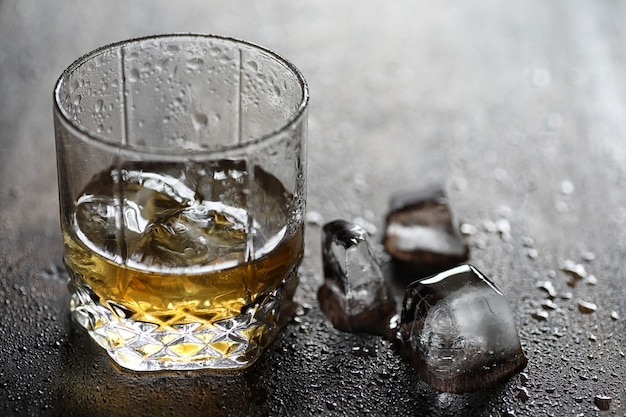 Whisky en un vaso y trozos de hielo sobre una mesa de madera