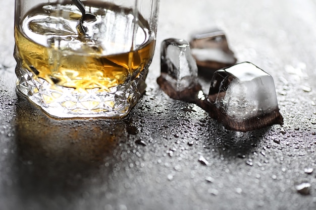 Whisky en un vaso y trozos de hielo sobre una mesa de madera